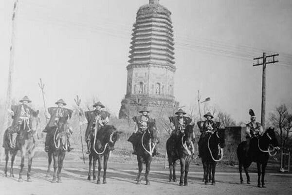 7 Chinese Gendarmes in peaked hats are mounted as skirmishes as cavalry in front of a temple. - Art Print