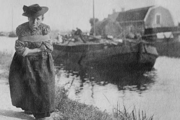 A Older Dutch woman has a bustle around her chest as she pulls a barge down a canal. - Art Print