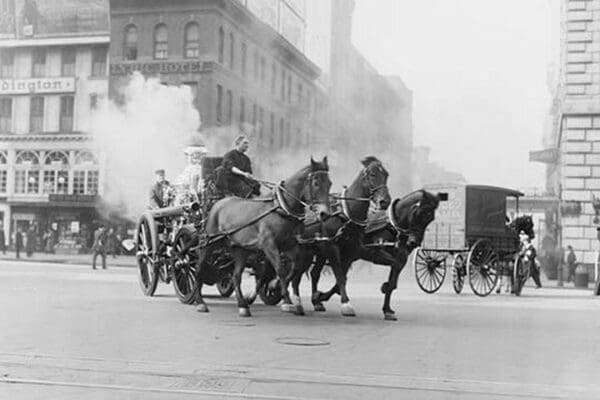 A Team of Horses pulls a steam pumper across paved streets toward a fire scene. - Art Print