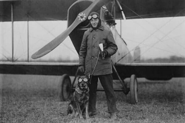 Aviator and His dog wear goggles in front of his Biplane - Art Print