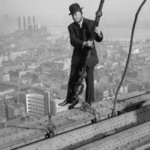 Cameraman in suit holds onto cable as he walks unharnessed over a skyscraper's steel girders - Art Print