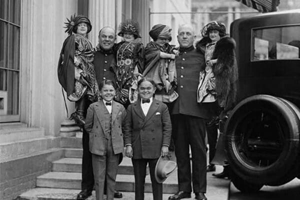 Little People all dressed in their finery are lifted in the arms of full sized people. - Art Print