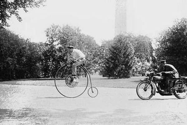 Motorcycle cop chases a Penny Farthing Velocipede down a DC Street with Washington Monument in background - Art Print